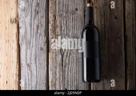 Dunkle Flasche teuren duftenden Rotweins auf Holzhintergrund. Konzept der Werbung und Promotion. Platz für Text. Flach liegend. Stockfoto