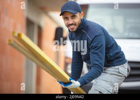 Fröhlicher Arbeiter, der Holz auf die Bebauung trägt Stockfoto