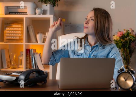 Junge Frau, die an ihrem Arbeitsplatz im Büro Darts spielt, mit Telefon- und Laptop-Hintergrund. Konzept von Arbeitsmomenten und Pausen. Stockfoto