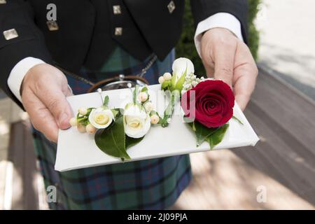 Nahaufnahme eines Mannes in einem schottischen Kilt, der mehrere Blumen für einen Hochzeitstag hält Stockfoto