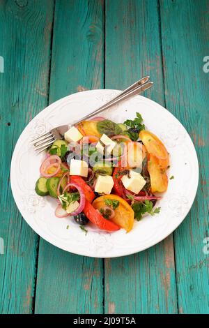 Frischer griechischer Salat mit rohem Gemüse und Feta-Käse in großer weißer Platte auf türkisfarbenem Tisch mit zwei Gabeln Copyspace Stockfoto