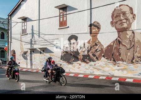 Motorräder in der Altstadt von Phuket passieren ein Wandgemälde zum Gedenken an König Bhumibol Adulyadej. Stockfoto