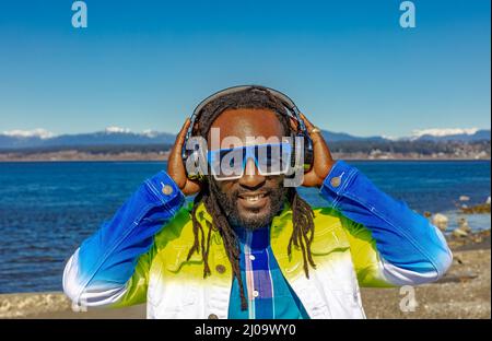 Hübscher attraktiver junger afroamerikanischer Mann mit Dreadlocks, der im Freien Musik hört. Straßenfoto. White Rock BC, Kanada, März 3,2022 Stockfoto