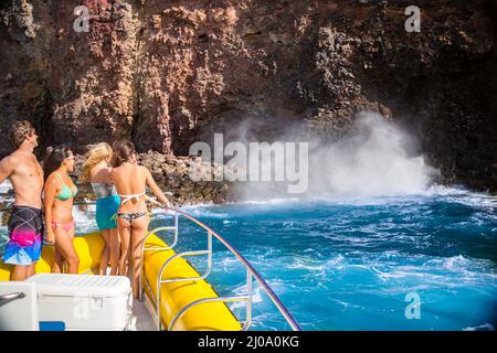 Eine Gruppe junger Menschen (MR) auf einem Schlauchboot mit hartem Boden und Blick auf ein Loch an der Küste entlang der Insel Lanai, Hawaii. Stockfoto