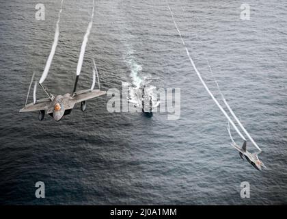 Die US Air Force F-22 Raptors, die der Alaska NORAD Region zugewiesen wurden, fliegen während der Operation NOBLE DEFENDER im Golf von Alaska am 16. März 2022 über den Lenkraketen-Zerstörer USS Curtis Wilbur. NOBLE DEFENDER ist eine Luftverteidigungsoperation des North American Aerospace Defense Command, bei der US-Streitkräfte mit Sicherheits- und Verteidigungspartnern zusammenarbeiten, um eine integrierte Abschreckung zu gewährleisten und Bedrohungen von allen möglichen Wegen aus zu schützen. (Foto DER US Air Force von Staff Sgt. Dylan Murakami) Stockfoto