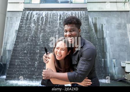 Zwei multiethnische Freunde umarmen sich mit einem fröhlichen Ausdruck im Freien Stockfoto