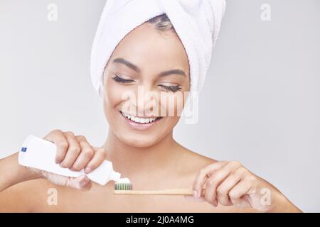 Scheut ein Fieber des Spaßes. Studioaufnahme einer schönen jungen Frau, die sich vor grauem Hintergrund die Zähne putzt. Stockfoto