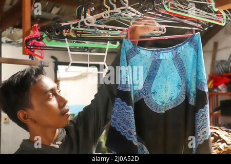 Asiatische Schneider hängen Poncho auf einem Kleiderbügel und Überprüfung der Qualität Stockfoto