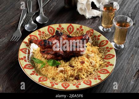 Hähnchen Dhum Biriyani mit Jeera-Reis und Gewürzen, serviert mit Tee. In Keramikplatte auf schwarzem rustikalem Holzhintergrund gerantet Stockfoto