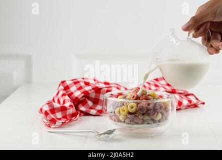 Gieße Milch in die Schüssel mit Froot Loops buntem Müsli. Frühstückskonzept Für Kinder, Kopierbereich Mit Weißem Hintergrund Stockfoto