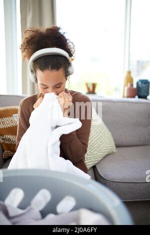 Nichts riecht besser als saubere Wäsche. Aufnahme einer Frau, die frisch gewaschene Wäsche riecht, während sie zu Hause sitzt. Stockfoto