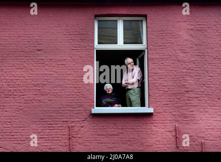 Ein älteres belgisches Paar, das vom Fenster seines Hauses in Brügge, Belgien, auf die Straße schaut. Stockfoto