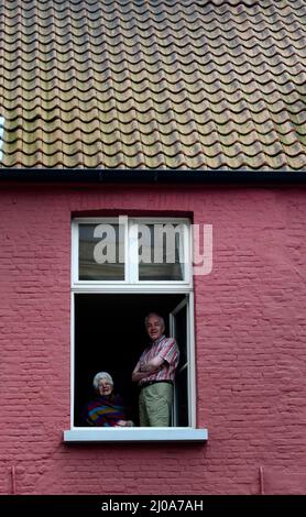 Ein älteres belgisches Paar, das vom Fenster seines Hauses in Brügge, Belgien, auf die Straße schaut. Stockfoto