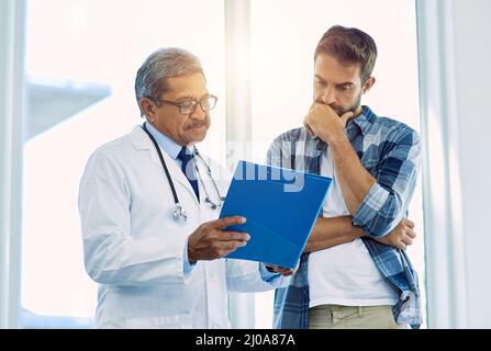 Es gibt ein paar Dinge, auf die Sie sich hier konzentrieren müssen. Aufnahme eines selbstbewussten reiferen männlichen Arztes, der einem Patienten im Krankenhaus während des Tests Testergebnisse zeigt Stockfoto