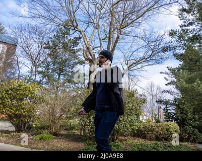 Seattle, WA USA - circa März 2022: Ein indischer Mann mit Mütze und Hoodie, der am Telefon telefoniert, während er in der Innenstadt von Seattle in der Nähe von The Space herumläuft Stockfoto