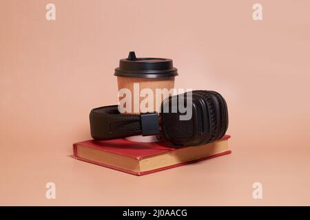 Hörbuch. Eine Papptasse Kaffee und Kopfhörer liegen auf einem Buch Stockfoto