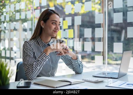 Glücklicher asiatischer Buchhalter, der im Büro sitzt und Kaffee hält. Stockfoto
