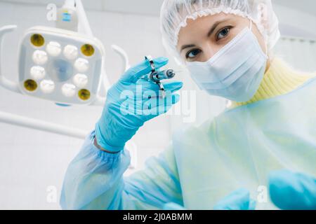 Ein maskierter Zahnarzt hält eine Injektionsspritze für einen Patienten im Büro. Stockfoto