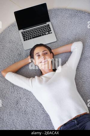 Lassen Sie meine Arbeit sich um sich selbst sorgen für eine Veränderung. Aufnahme einer jungen Frau, die auf einem Teppich neben einem Laptop liegt. Stockfoto