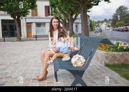 Kleiner, hübscher Junge aus dem Osten und ihre Mutter, die zusammen spielen und draußen auf der Bank sitzen Stockfoto