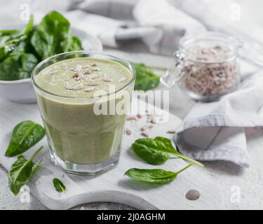 Ein Glas hausgemachter gesunder grüner Smoothie mit frischem Babyspinat, Sonnenblumen und Sesamsamen auf hellem Hintergrund. Essen und Trinken, Diät und gesund Stockfoto