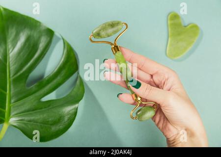 Weibliche Hand hält Massagerolle für das Gesicht mit zwei Köpfen aus grünem Jadestein. Schönheitsmassage im Gesicht, SPA-Selbstpflege-Konzept. Stockfoto