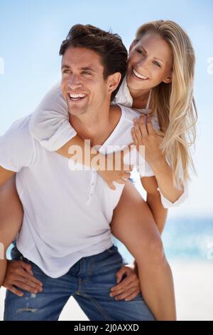 Spaß in der Sonne. Ein hübscher, junger Freund, der seiner Freundin eine Huckepack-Fahrt am Strand gibt. Stockfoto