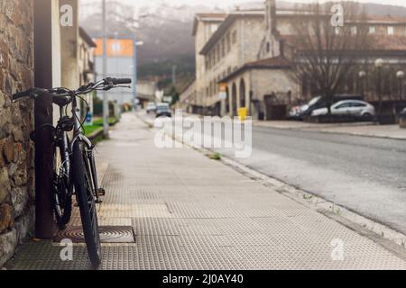 Fahrrad auf dem Bürgersteig in der Nähe der Stadtstraße in Spanien geparkt. Fahrrad auf Stange neben dem alten Gebäude lehnen. Vorderansicht des Fahrrads auf verschwommenem Gebäude, Autofahren Stockfoto