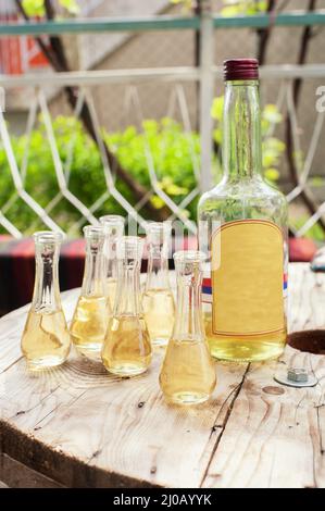 Flasche Pflaumenbrand mit kleinen Gläsern auf Holztisch. Außenaufnahme Stockfoto