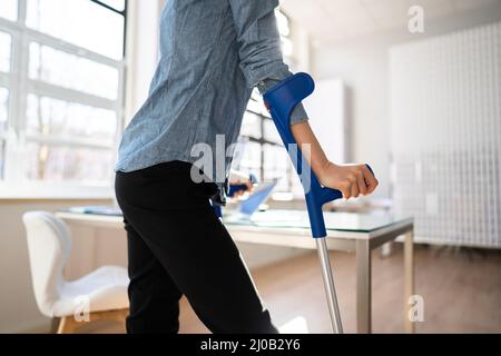 Arbeiter Mit Krücken Am Arbeitsplatz Oder Im Büro. Leistungen Für Die Rehabilitation Bei Handicap Stockfoto