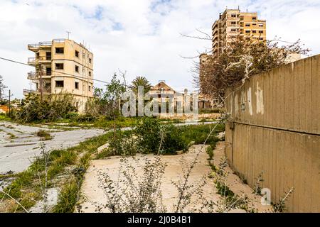 Der Bezirk Varosha (Kapalı Maraş) in Famagusta (Zypern) war zwischen 1970 und 1974 eines der beliebtesten Reiseziele der Welt. Die griechisch-zyprischen Einwohner flohen 1974 während der türkischen Invasion auf Zypern, als die Stadt Famagusta unter türkische Kontrolle kam. Seither ist sie verlassen und die Gebäude sind verfallen. Die meisten der ursprünglichen Bewohner von Varosha (und ihre direkten Nachkommen) leben heute südlich der UN-Pufferzone Zyperns. Diese Familien sind immer noch die legalen Eigentümer von Eigentum in Varosha, aber während die Stadt umkämpft wird, können sie es nicht zurückfordern. Und viele Stockfoto