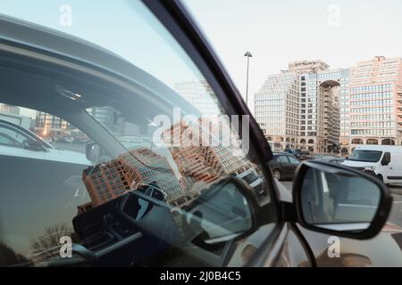 Die urbane Landschaft spiegelte sich im Autospiegel wider. Außenansicht typischer moderner Apartmentgebäude vor einem blauen Himmel mit Wolken Stockfoto