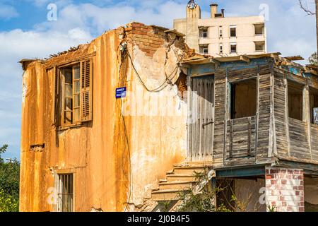 Der Bezirk Varosha (Kapalı Maraş) in Famagusta (Zypern) war zwischen 1970 und 1974 eines der beliebtesten Reiseziele der Welt. Die griechisch-zyprischen Einwohner flohen 1974 während der türkischen Invasion auf Zypern, als die Stadt Famagusta unter türkische Kontrolle kam. Seither ist sie verlassen und die Gebäude sind verfallen. Die meisten der ursprünglichen Bewohner von Varosha (und ihre direkten Nachkommen) leben heute südlich der UN-Pufferzone Zyperns. Diese Familien sind immer noch die legalen Eigentümer von Eigentum in Varosha, aber während die Stadt umkämpft wird, können sie es nicht zurückfordern. Und viele Stockfoto