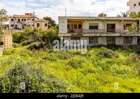 Der Bezirk Varosha (Kapalı Maraş) in Famagusta (Zypern) war zwischen 1970 und 1974 eines der beliebtesten Reiseziele der Welt. Die griechisch-zyprischen Einwohner flohen 1974 während der türkischen Invasion auf Zypern, als die Stadt Famagusta unter türkische Kontrolle kam. Seither ist sie verlassen und die Gebäude sind verfallen. Die meisten der ursprünglichen Bewohner von Varosha (und ihre direkten Nachkommen) leben heute südlich der UN-Pufferzone Zyperns. Diese Familien sind immer noch die legalen Eigentümer von Eigentum in Varosha, aber während die Stadt umkämpft wird, können sie es nicht zurückfordern. Und viele Stockfoto