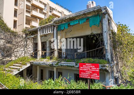 Der Bezirk Varosha (Kapalı Maraş) in Famagusta (Zypern) war zwischen 1970 und 1974 eines der beliebtesten Reiseziele der Welt. Die griechisch-zyprischen Einwohner flohen 1974 während der türkischen Invasion auf Zypern, als die Stadt Famagusta unter türkische Kontrolle kam. Seither ist sie verlassen und die Gebäude sind verfallen. Die meisten der ursprünglichen Bewohner von Varosha (und ihre direkten Nachkommen) leben heute südlich der UN-Pufferzone Zyperns. Diese Familien sind immer noch die legalen Eigentümer von Eigentum in Varosha, aber während die Stadt umkämpft wird, können sie es nicht zurückfordern. Und viele Stockfoto