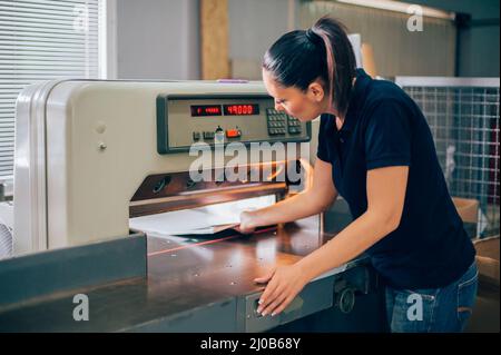 Papierzuschneidemaschine. Arbeiter in einem Druck- und Druckmaschinencentar verwendet industrielle Messerschneidemaschine Stockfoto