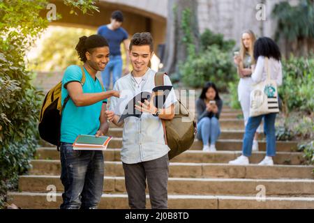 Zwei junge männliche multirassische Studenten, die auf einigen Treppen ein Notizbuch angeschaut haben Stockfoto