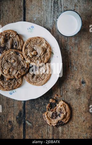 Chocolate Chip Cookies und ein Glas Milch auf einem Holztisch Stockfoto