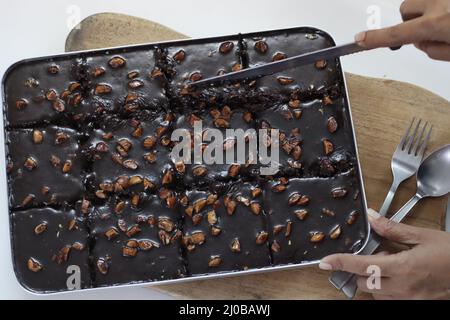 Schneiden von Texas Torte. Butterhaltiger und schokoladiger Kuchen in rechteckige Stücke im Backblech geschnitten. Frisch aus dem Ofen. Aufgenommen auf weißem Hintergrund Stockfoto