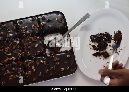 Ein Stück Texas-Torte auf einem Teller serviert. Butterhaltiger und schokoladiger Kuchen in rechteckige Stücke im Backblech geschnitten und daraus geschöpft. Aufnahme o Stockfoto