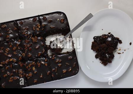 Ein Stück Texas-Torte auf einem Teller serviert. Butterhaltiger und schokoladiger Kuchen in rechteckige Stücke im Backblech geschnitten und daraus geschöpft. Aufnahme o Stockfoto