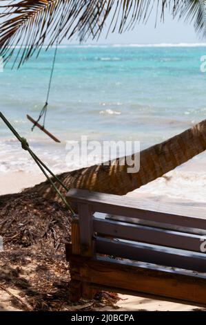 Hölzerne Bank Swing neben einer Palme vor dem Ozean Karibik weißen Sandstrand auf der Insel little Corn island Stockfoto