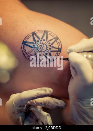 Master Tattoo zeichnet die blaue Farbe auf dem Kunden Tattoo Stockfoto