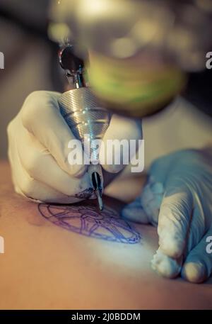 Master Tattoo zeichnet die blaue Farbe auf dem Kunden Tattoo Stockfoto