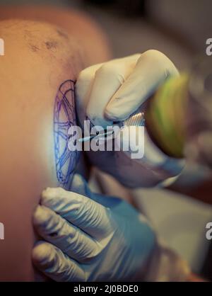 Master Tattoo zeichnet die blaue Farbe auf dem Kunden Tattoo Stockfoto