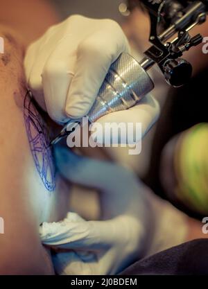 Master Tattoo zeichnet die blaue Farbe auf dem Kunden Tattoo Stockfoto