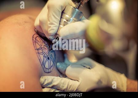 Master Tattoo zeichnet die blaue Farbe auf dem Kunden Tattoo Stockfoto