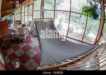 Weiße große Hängematte und Rattan-Möbel auf Fliesenboden in einem hostel Stockfoto