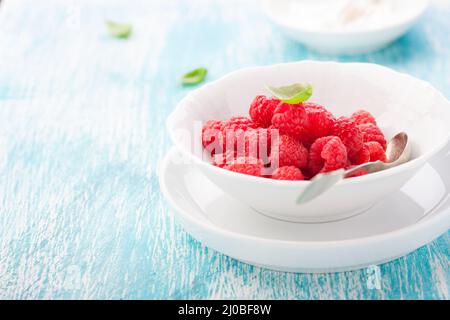 Frische Himbeeren in einer weißen Keramikschale mit Metalllöffel. Stockfoto