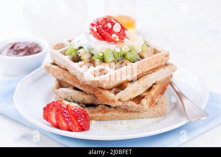 Waffeln mit Vollkornmehl und Früchten auf einem weißen Teller auf einer blauen Serviette Stockfoto